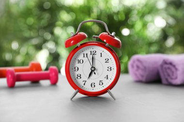 Alarm clock, towels and dumbbells on grey table against blurred background. Morning exercise