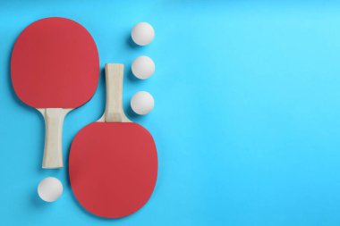 Ping pong rackets and balls on light blue background, flat lay. Space for text