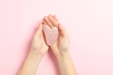 Woman with rose quartz gua sha tool on light pink background, closeup