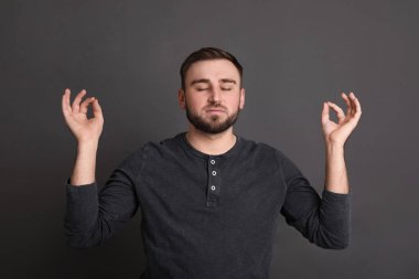 Young man meditating on grey background. Personality concept