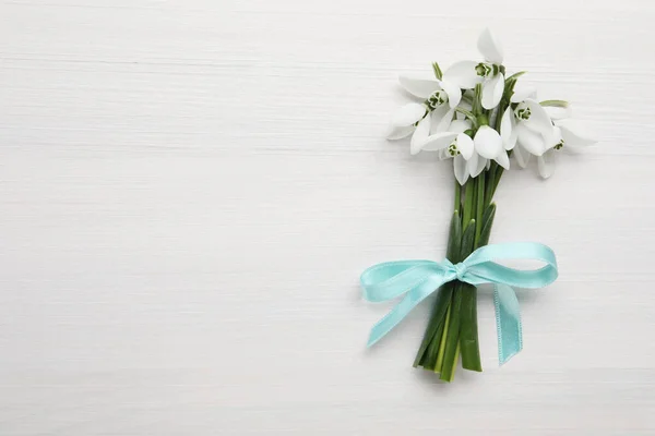 Beautiful snowdrop flowers with ribbon on white wooden table, top view. Space for text