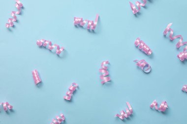 Shiny pink serpentine streamers light blue background, flat lay