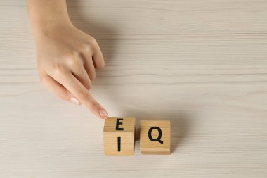 Woman turning cube with letters E and I near Q at white wooden table, above view. Space for text