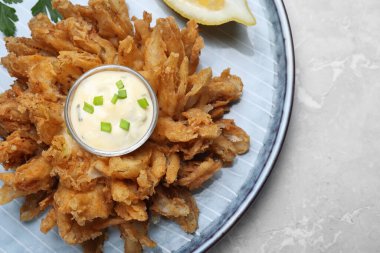 Fried blooming onion with dipping sauce served on light marble table, top view