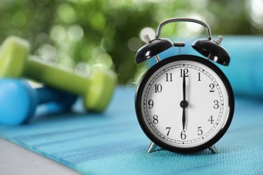 Alarm clock on yoga mat against blurred background. Morning exercise