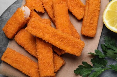 Fresh breaded fish fingers, parsley and lemon on black board, top view