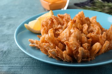 Kızarmış soğan mavi ahşap masada servis edilir, yakın plan.