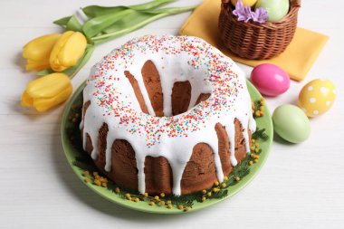 Beyaz ahşap masaya serpiştirilmiş Paskalya pastası, boyanmış yumurtalar ve çiçekler.