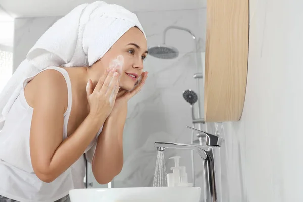 Happy mature woman washing face in bathroom