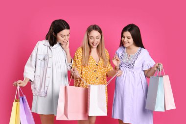 Pembe arka planda alışveriş torbaları olan mutlu hamile kadınlar.