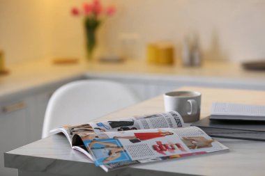 Open fashion magazine and drink on table in kitchen. Space for text clipart