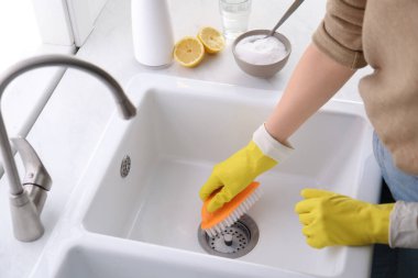 Woman using baking soda and brush to clean sink, closeup clipart