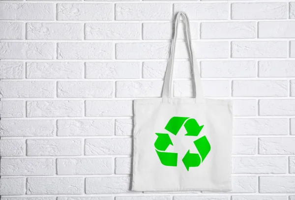 Bag with recycling symbol hanging on brick wall. Space for text