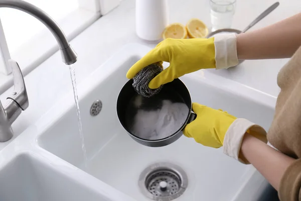 Woman using baking soda and metal sponge to clean pot, closeup
