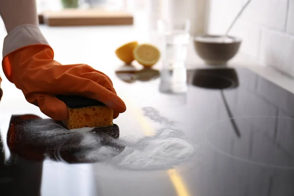 Woman using baking soda to clean electric cooktop indoors, closeup. Wrong detergent for such surfaces