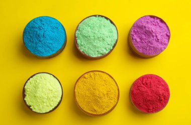 Sarı arka planda kaselerde renkli tozlar, düz bir zemin. Holi festivali kutlaması