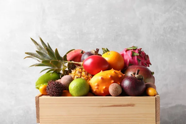 Crate with different exotic fruits on light grey background
