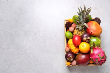 Açık gri masada değişik egzotik meyveler olan sandık, üst manzara. Metin için boşluk