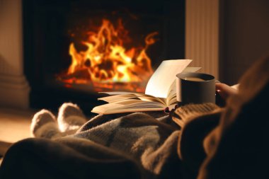 Elinde bir bardak içki ve kitap olan kadın şöminenin yanında, yakın çekim.