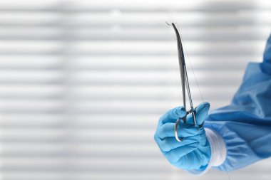 Doktor dikiş ipliği olan iğneyi içeride tutuyor, yakın plan ve metin için boşluk. Tıbbi ekipman