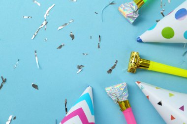 Parlak parti şapkaları, boynuzlar ve açık mavi arka planda konfeti, düz yatış