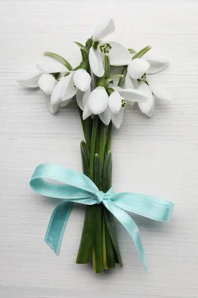 Beautiful snowdrop flowers with ribbon on white wooden table, top view