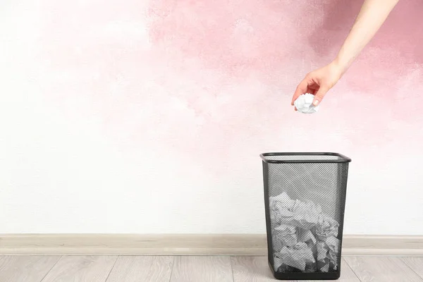 Woman throwing crumpled paper ball into basket near pink wall, closeup. Space for text