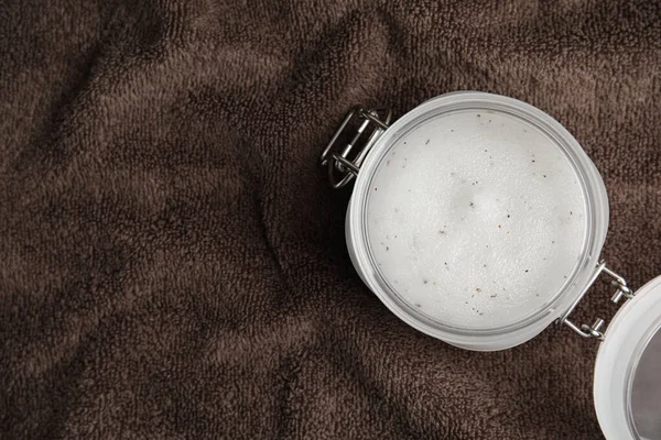 Jar of salt scrub on brown towel, top view. Space for text
