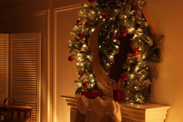 Mirror with Christmas garland and fairy lights over fireplace in room