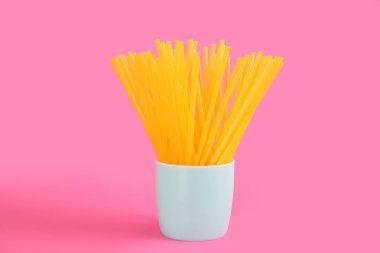 Sarı plastik pipetler pembe arka planda duruyor.