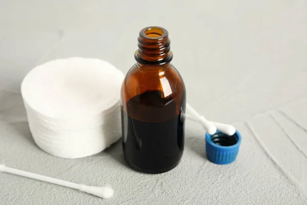 Bottle of medical iodine, cotton pads and buds on grey table