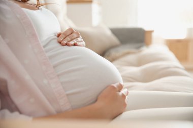 Hamile kadın karnına dokunuyor. Kapalı mekanda.