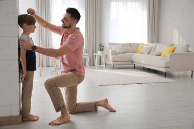 Baba, evdeki duvarın yanında oğlunun boyunu ölçüyor.