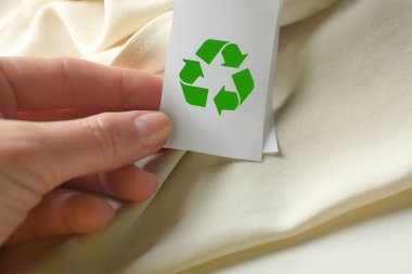 Bej elbisenin üzerinde geri dönüşüm sembolü olan kıyafet etiketi gösteren kadın, yakın plan.