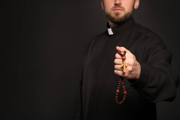 Священник с четками на черном фоне, крупным планом. Пространство для текста