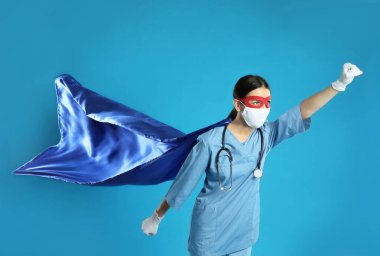 Açık mavi arka planda süper kahraman gibi giyinmiş bir doktor. COVID-19 ile savaşan tıp çalışanları kavramı