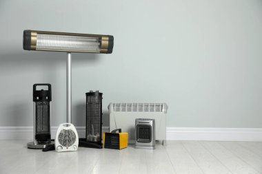 Açık gri duvarın yanında farklı elektrikli ısıtıcılar var. Metin için boşluk