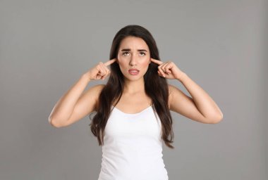 Gri arka planda kulakları olan duygusal genç bir kadın.