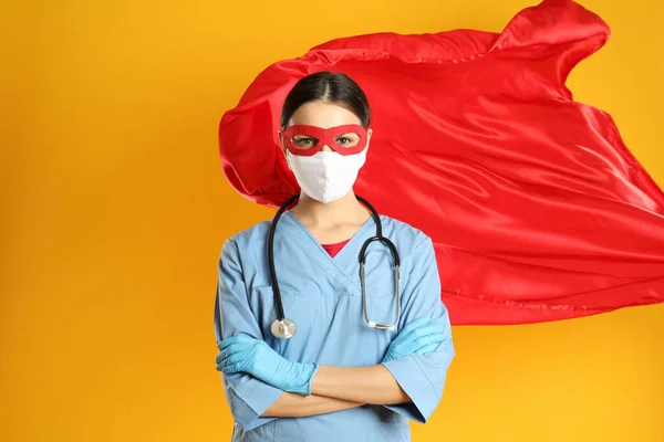 Doctor dressed as superhero posing on yellow background. Concept of medical workers fighting with COVID-19