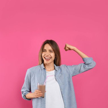 Bir bardak çikolatalı sütle genç bir kadın pembe arka planda gücünü gösteriyor.