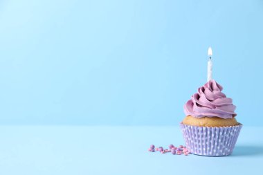 Lezzetli doğum günü keki yanan mum ve açık mavi arkaplan üzerine serpiştirilmiş şekerlemeler, metin için boşluk