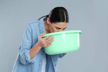Woman with basin suffering from nausea on grey background. Food poisoning clipart