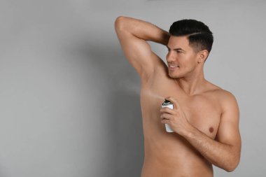 Gri arka planda koltukaltına deodorant uygulayan yakışıklı adam, metin için boşluk