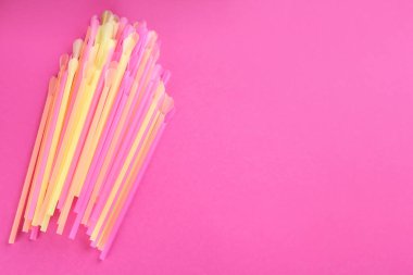 Pembe arka planda renkli plastik pipetler, düz yatış. Metin için boşluk