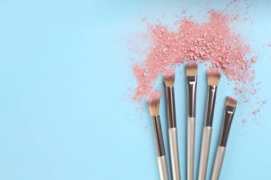 Makyaj fırçaları ve göz farları açık mavi arka planda, düz yerde. Metin için boşluk