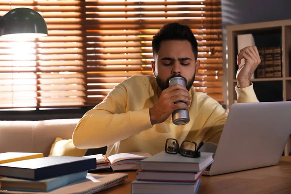 Tired young man with energy drink studying at home