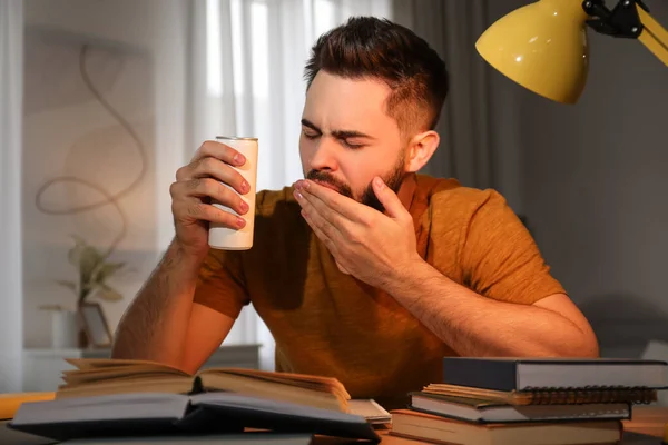 Tired young man with energy drink studying at home