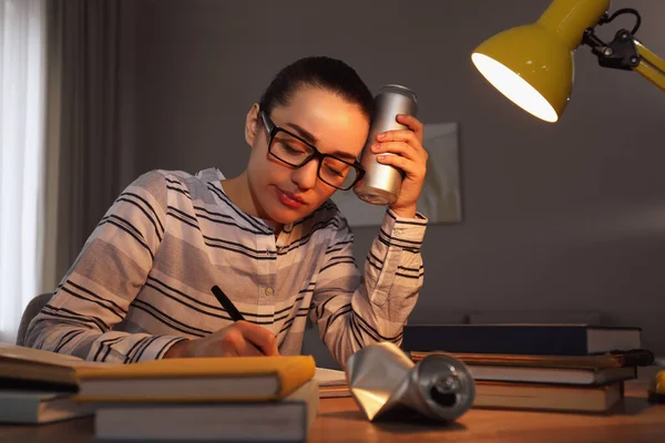 Tired young woman with energy drink studying at home