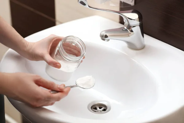 Woman using baking soda to unclog sink drain in bathroom, closeup