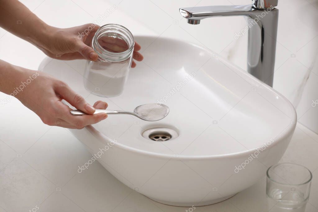 Woman using baking soda to unclog sink drain in bathroom, closeup